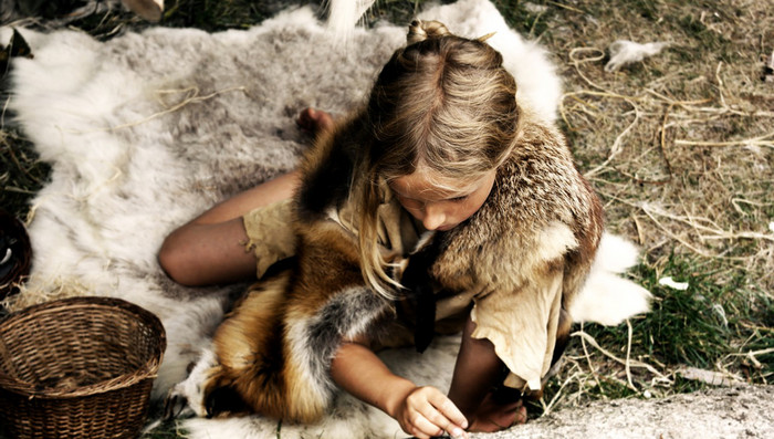 Ein in Fell gekleidetes Kind in der Steinzeit ritzt ein Bild in einen Stein.