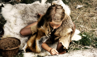 Ein in Fell gekleidetes Kind in der Steinzeit ritzt ein Bild in einen Stein.