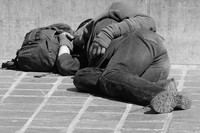 Ein schlafender Mann liegt mit Rucksack auf dem Fußweg