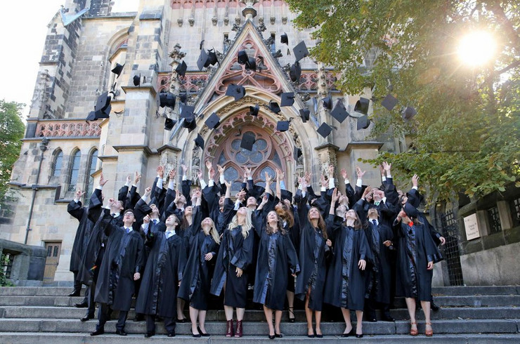 Junge Absolventen werfen ihre Magisterhüte in die Luft vor der Thomaskirche.