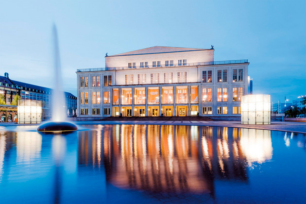 Die Oper Leipzig in der Abenddämmerung mit Wasserfläche und Springbrunnen im Vordergrund