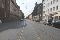 Das Foto zeigt den Straßenquerschnitt der Ratzelstraße in Höhe der Einmündung Hermann-Meyer-Straße: Gleisanlagen, Fahrbahn, Parkstellflächen und Gehwege. Die Fahrbahn weist großflächige Rissbildungen sowie Schlaglöcher auf.