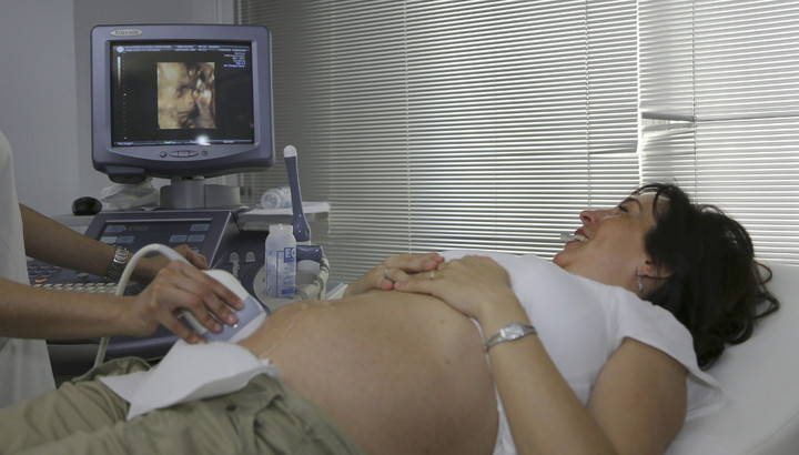Eine schwangere Frau liegt auf einer Liege. Ihr Bauch wird per Ultraschall untersucht.