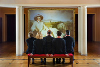 Fünf Menschen in dunklen Anzügen sitzen auf einer Band und blicken auf ein Gemälde mit Johann Wolfgang von Goethe.