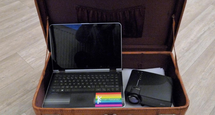 Ein Laptop und ein Beamer in einem geöffneten, alten Reisekoffer
