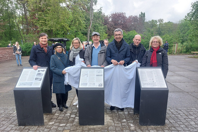 Eine Reihe von Menschen stehen mit Decke in der Hand hinter den enthüllten Gedenktafeln im Leipziger Mariannenpark.