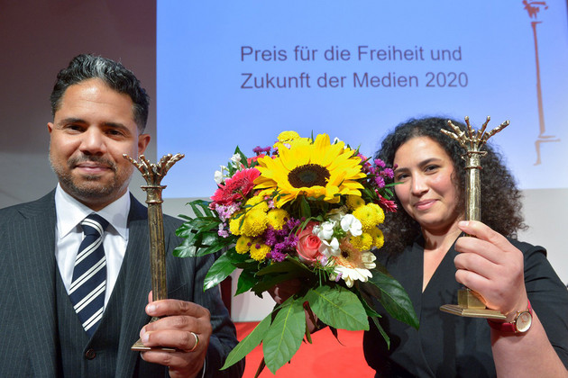 Eine Frau und ein Mann halten jeweils einen Preis und Blumen in der Hand.