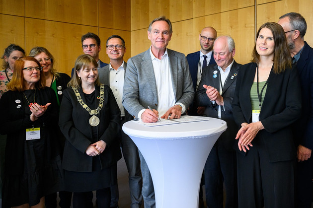 Oberbürgermeister Burkhard Jung unterzeichnet ein Papier, umgeben von vielen Personen.