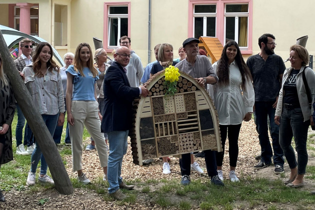 Eine Menschengruppe steht vor dem Haus und hält das neue Insektenhotel in den Händen
