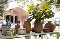 Verschiedene Keramikobjekte stehen auf einem Tisch, im Hintergrund Menschen, die über den Markt schlendern.