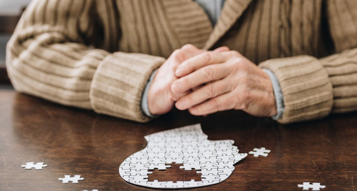 Ältere Frau sitzt mit verschränkten Händen an einem Tisch und puzzelt