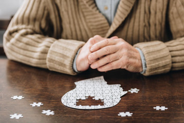 Ältere Frau sitzt mit verschränkten Händen an einem Tisch und puzzelt