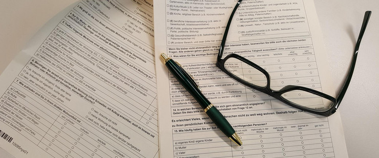 Fragebogen auf einem Tisch, darauf liegen ein Stift und eine Brille.