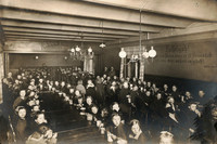 Viele Kinder aber auch Erwachsene in einem Saal an Tischen mit Essgeschirr im Jahr 1923.
