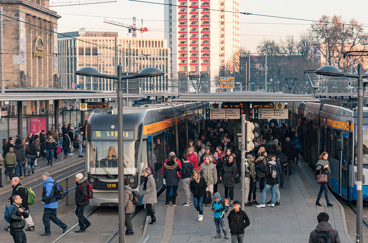 Haltestelle der Leipziger Verkehrsbetriebe am Leipziger Hauptbahnhof mit zwei haltenden Straßenbahnen und vielen Menschen, die ein- und aussteigen.