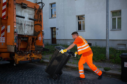 Ein Mitarbeiter der Stadtreinigung Leipzig fährt eine Mülltonne zum Abfallentsorgungsauto