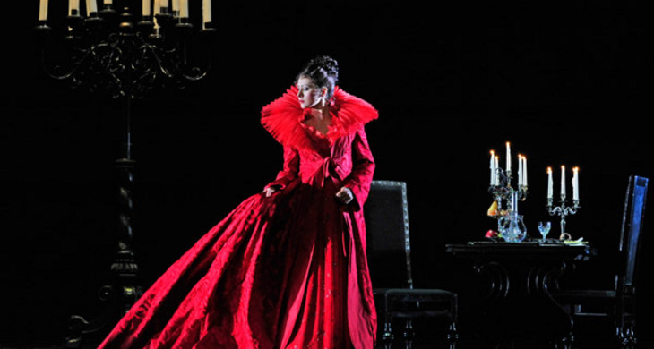 Szene aus Tosca in der Oper Leipzig: Frau in rotem langen Kleid auf dunkler Bühne