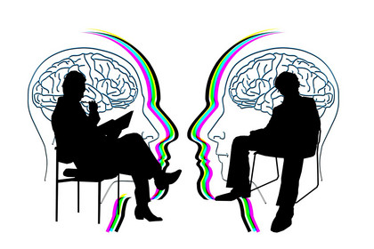 Zwei Menschen sitzen sich auf einem Stuhl gegenüber und sprechen miteinander. Im Hintergrund sind Shilouetten zwei sich zugewandter Köpfe zu sehen.