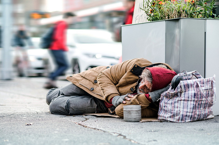 Obdachloser Mensch liegt mit seinen Taschen auf dem Bürgersteig und bittet um Spenden