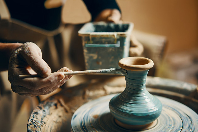 Eine Person malt mit einem Pinsel eine Vase auf einer Töpferscheibe an
