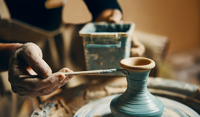 Eine Person malt mit einem Pinsel eine Vase auf einer Töpferscheibe an