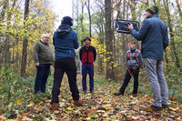 Fünf Menschen stehen im Wald im Kreis und sprechen, einer hat eine Kamera