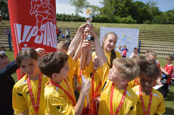 Mehrere Jungen und Mädchen in gelben T-Shirts halten gemeinsam einen Pokal in die Höhe.