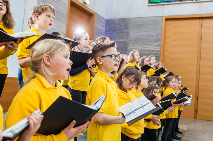 Singende Kinder in gelben T-Shirts mit Gesangsbüchern