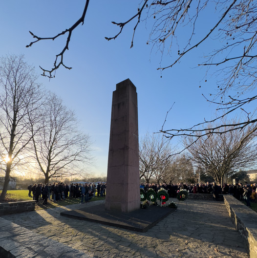 Rückseite des Mahnmals in Abnaundorf mit vielen Menschen bei einer Gedenkveranstaltung.