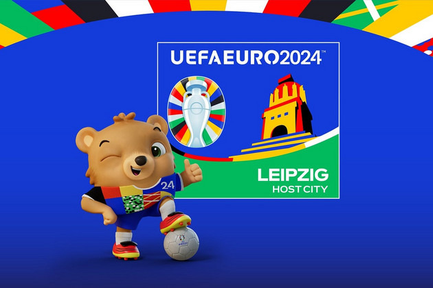 Ein animierter Bär steht mit einem Fußball vor dem Host-City-Logo der Stadt Leipzig.
