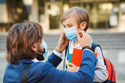 Vater hilft seinem Sohn vor der Schule eine OP-Maske aufzusetzen.