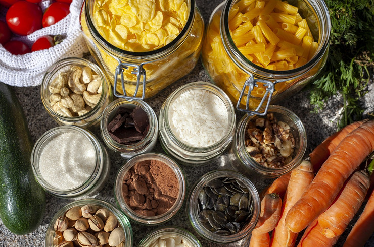 Verschiedene Behälter mit Nüssen, Nudeln, Reis und anderen Lebensmitteln sowie loses Gemüse