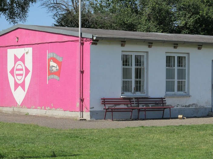 Sozialgebäude des Erich-Steinfurth-Stadion mit einer rosa gestrichen Wand auf der Vereinslogos prangen.