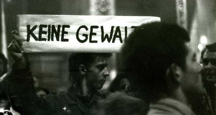 Eine junger Mann hält ein Schild während einer Demonstration im Herbst 89 hoch. Auf dem Schild steht "Keine Gewalt"