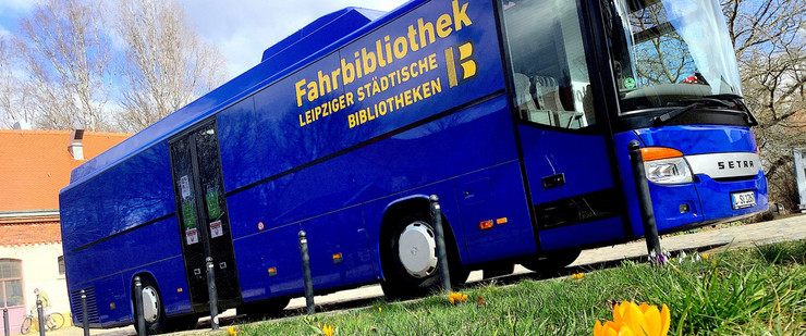 Blauer Bus mit gelber Beschriftung Fahrbibliothek steht vor einer grünen Wiese mit gelben Blumen