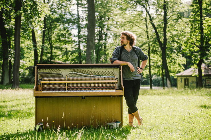 Ein Mann steht an ein klavierähnliches Instrument gelehnt auf einer grünen Wiese