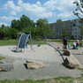 Generationenpark Schönefeld Grünfläche mit Spielgeräten. Im Hintergrund sind Plattenbauten sichtbar.