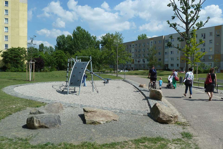 Generationenpark Schönefeld Grünfläche mit Spielgeräten. Im Hintergrund sind Plattenbauten sichtbar.