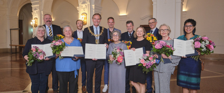 Gruppenbild der Preisträgerinnen und Preisträger der Goldenen Ehrennadel 2023 mit ihren Urkunden und Blumensträußen und Oberbürgermeister Burkhard Jung im Neuen Rathaus