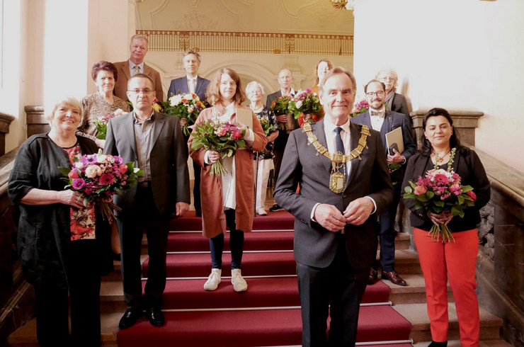 Auf einer Treppe stehen 13 Frauen und Männer und blicken in die Kamera. Sie halten Urkunden und Blumensträuße in ihren Händen.