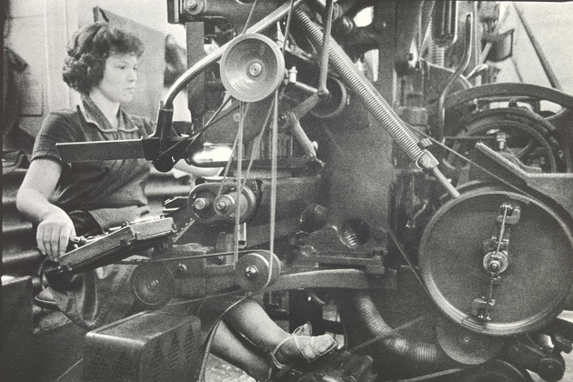 Schwarz-Weiß-Foto mit einer jungen Frau, die an einer Druckmaschine arbeitet.