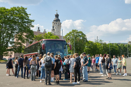 Eine große Gruppe Jugendlicher vor einem Reisebus, im Hintergrund das Neue Rathaus