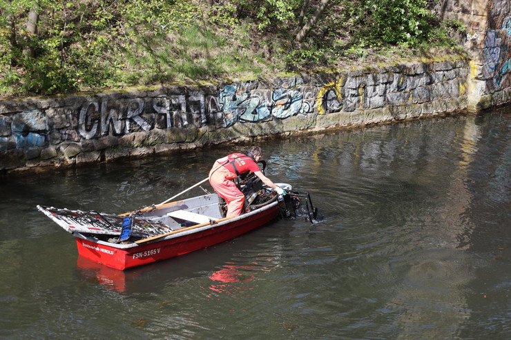 Eine Person steht auf einem Boot und zieht ein altes Fahrrad aus dem Wasser.