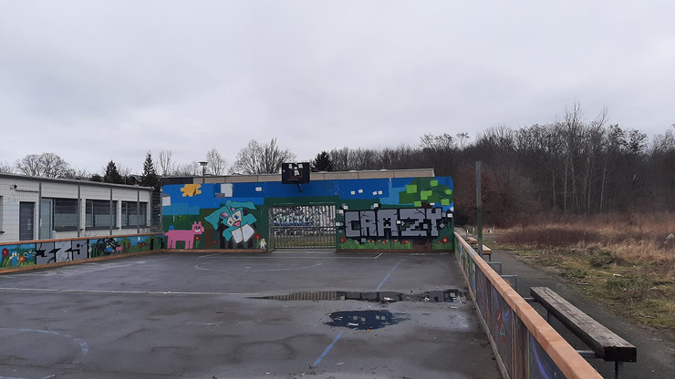 Am hinteren Ende eines Basketballspielfeldes wurde eine Mauer mit Graffiti gestaltet. Das Wort Crazy fällt ins Auge.