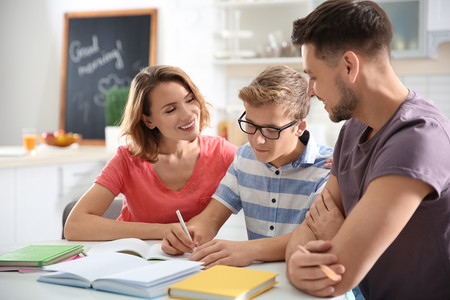 Mutter, Junge und Vater sitzen an einem Tisch und machen zusammen Hausaufgaben.