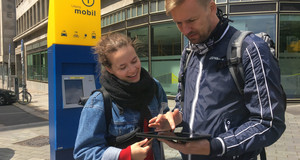 Eine Frau und ein Mann stehen mit einem Tablet in der Hand vor einem Service-Center der Leipziger Verkehrsbetriebe.