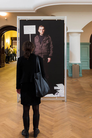 Eine Frau steht vor einem schwarzen Ausstellungsbanner mit einer Frau drauf.