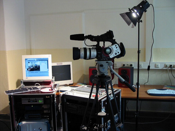 Eine Videokamera mit einem Scheinwerfer vor einem Mischpult und einem Video-Schnitt-Rechner
