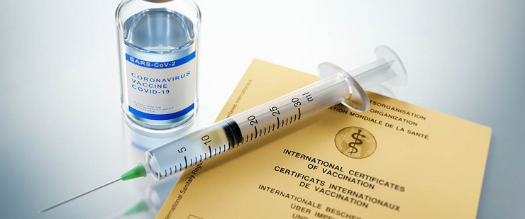 Eine Spritze neben einem kleinen Glasbehälter für Corona-Impfstoff und einem Impfpass