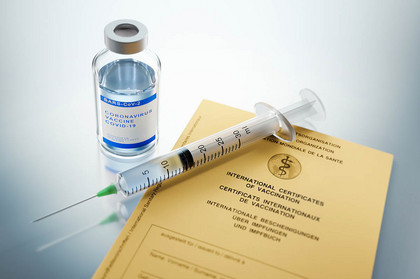 Eine Spritze neben einem kleinen Glasbehälter für Corona-Impfstoff und einem Impfpass